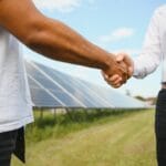 Deux hommes faisant une poignée de mains devant des panneaux solaires