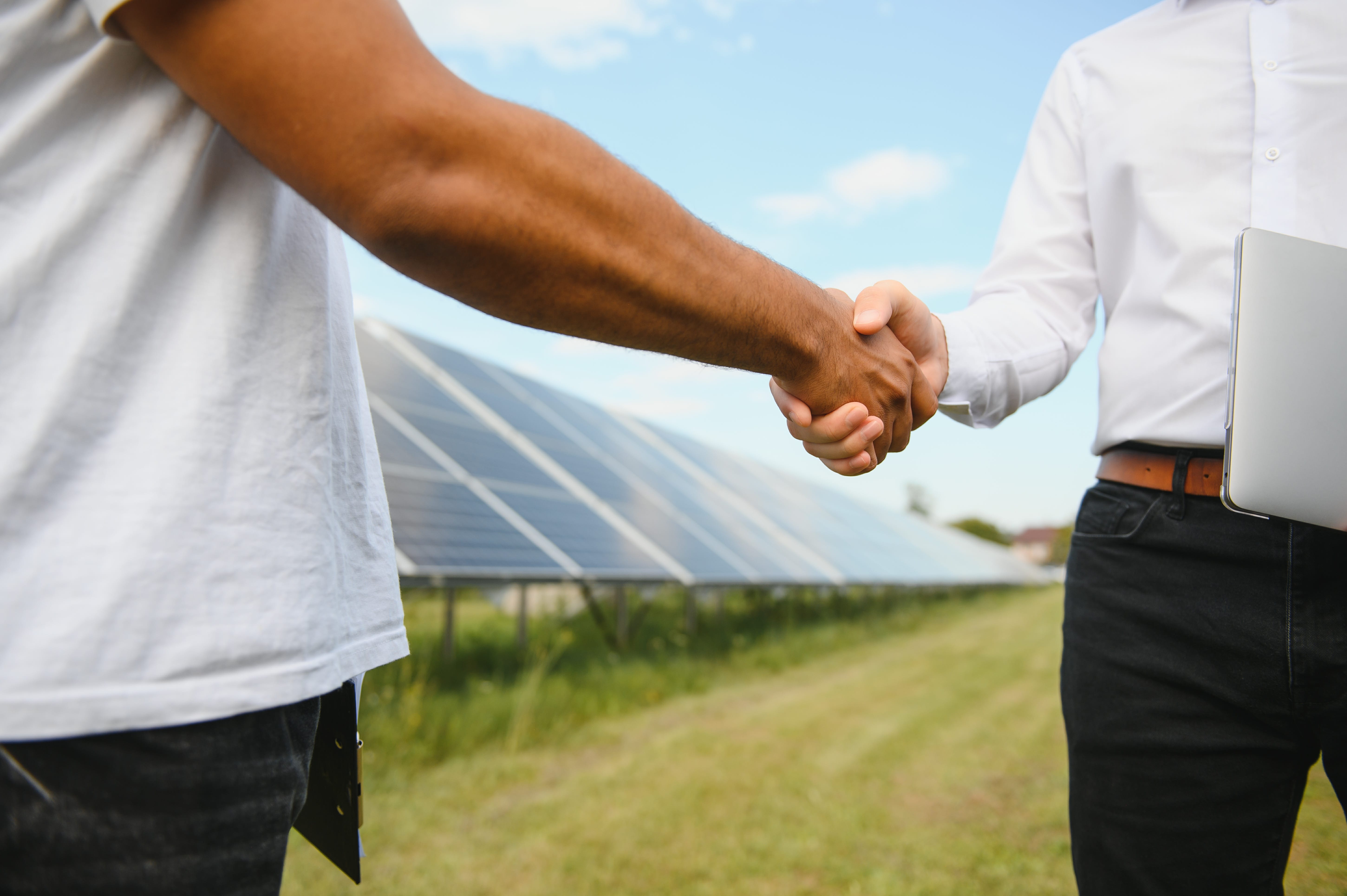 Deux hommes faisant une poignée de mains devant des panneaux solaires