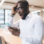 Un homme surpris lit des frais cachés de forfaits mobiles sur son smartphone