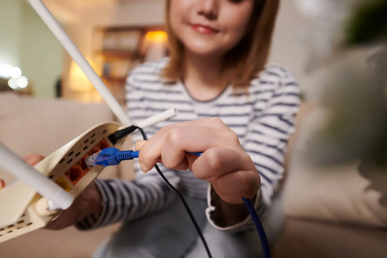 une femme dans son appartement connectant un câble Ethernet à sa box WiFi afin d'avoir une meilleure connexion
