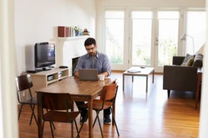 homme assis à la table à manger dans son salon étudiant son éligibilité fibre et les offres existantes sur son ordinateur portable
