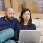 un couple au milieu des cartons de déménagement compare les offres de contrat d'électricité avant leur emménagement